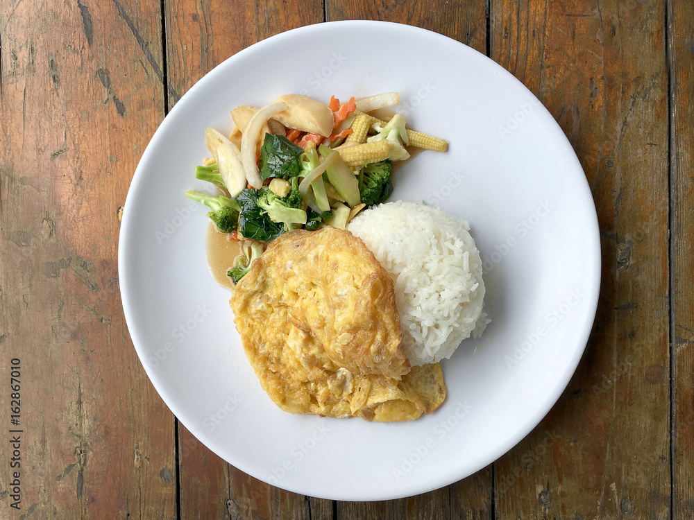 Vegetable stir fry with Omelette in a white plate on wooden background. Thai style food. Vegetarian Food Vegetable stir fry with Omelette in a white plate on wooden background. Thai style food. Vegetarian Food