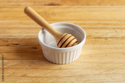 wooden honey dipper and white ceramic bowl on wooden table