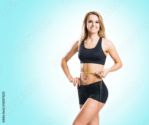 Fit, healthy and sporty woman in sportswear measuring her body over cyan background.