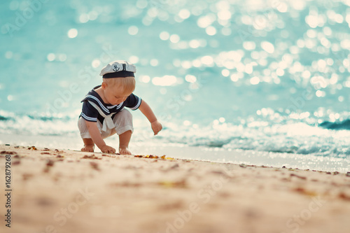 little boy walking at the beach in straw hat