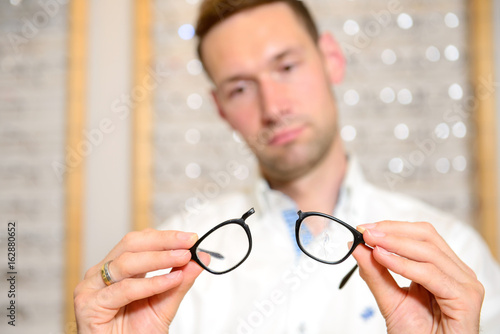 in optician shop- young man with broken glasses