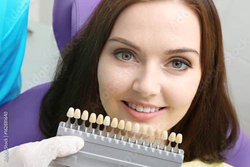 Dentist checking and selecting color of young woman teeth