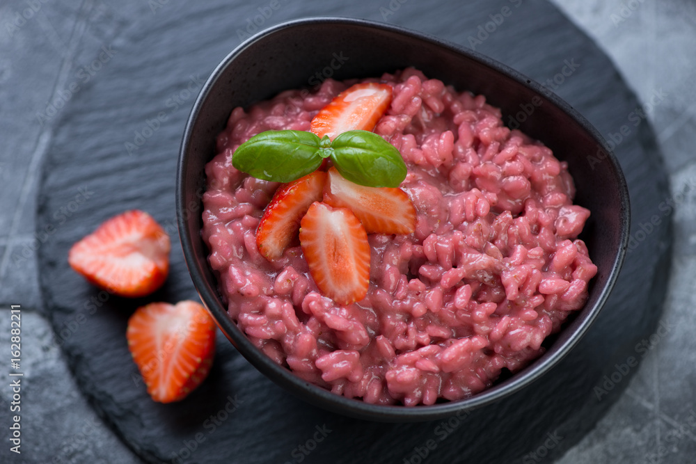 Risotto with strawberries served in a black bowl on a stone slate tray, close-up, elevated view Risotto with strawberries served in a black bowl on a stone slate tray, close-up, elevated view