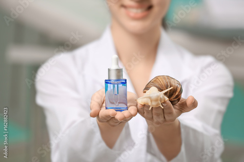 Young woman with giant Achatina snail and cosmetic product, closeup