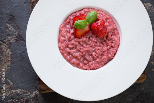 Above view of a white plate with strawberry risotto over brown stone background, horizontal shot