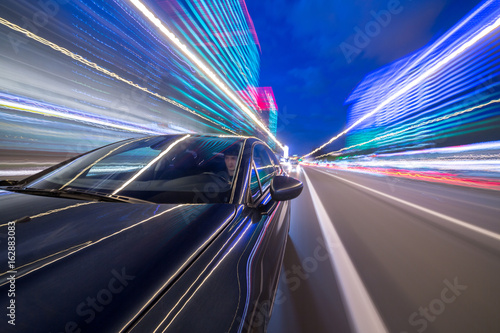View from Side of Car moving in a night city, Blured road with lights with car on high speed. Concept rapid rhythm of a modern city.
