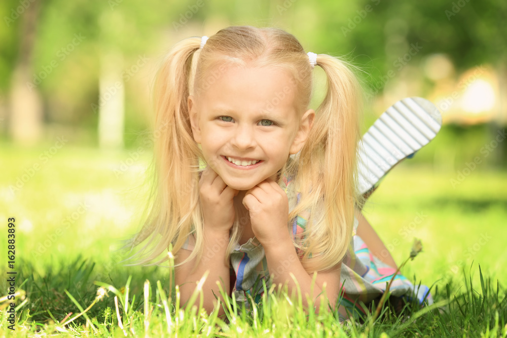 Cute little girl lying on green grass in park Cute little girl lying on green grass in park