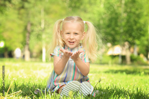 Cute little girl sitting on green grass in park © Africa Studio