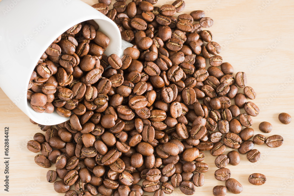 Fototapeta premium White ceramic coffee cup filled with the coffee beans on wooden table.