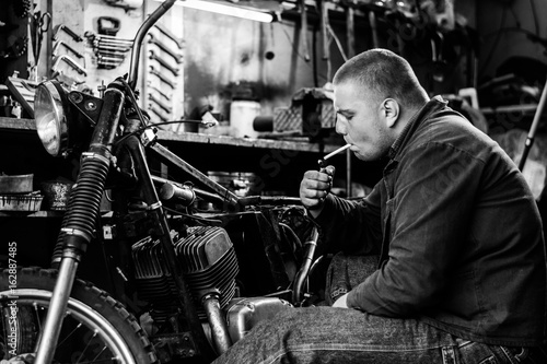 Man smoke during a break of repairing old motorcycle in workshop