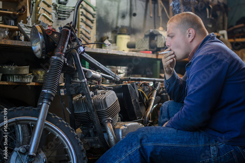 Man smoke during a break of repairing old motorcycle in workshop