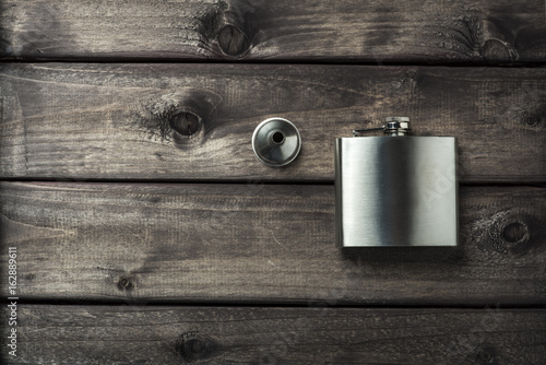 Metall hip flask with cup on wooden backdrop