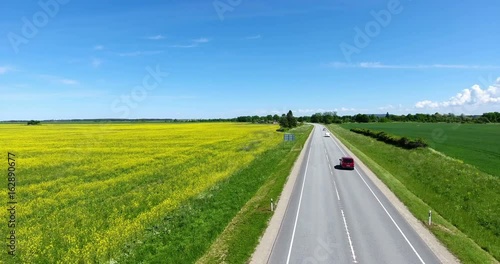 Flying across country highway in blooming meadows. Vehicles driving on road