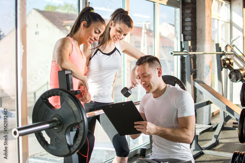 Gym instructor assisting two sporty women with in fitness center.