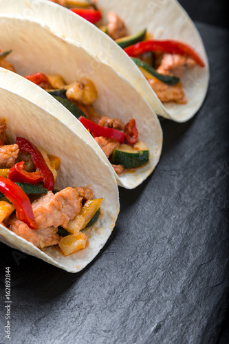 Mexican tacos with pork and vegetables. Al pastor taco on slate tableware. Close up.