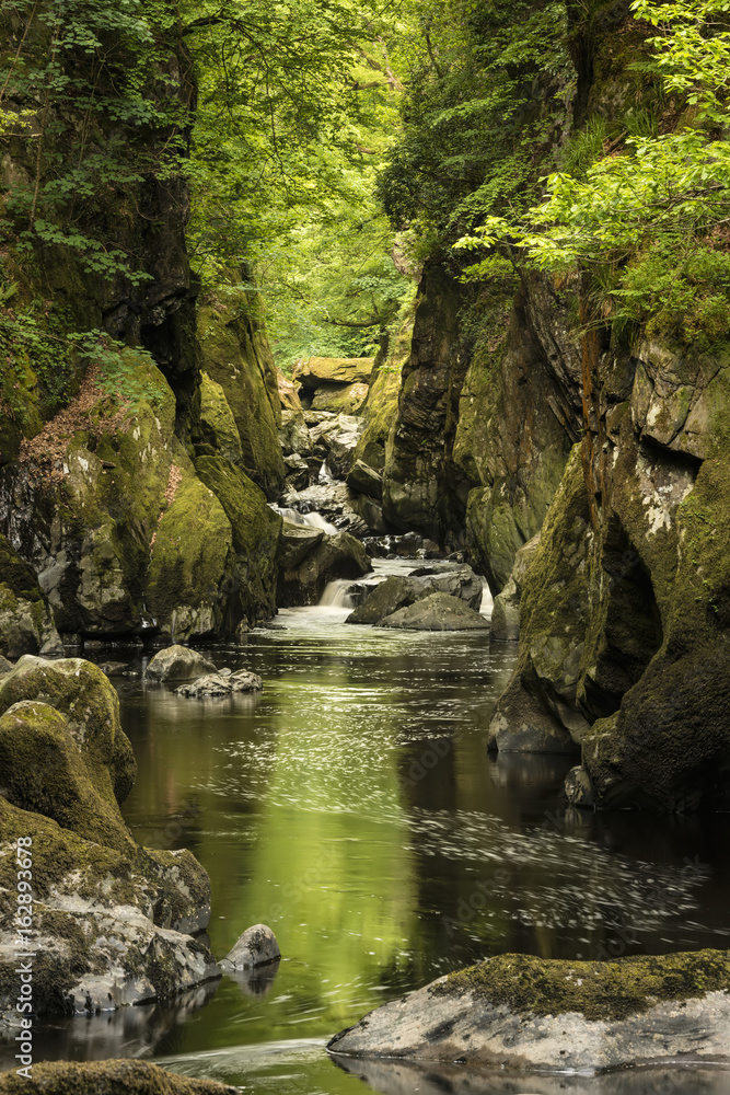 Stunning ethereal landscape of deep sided gorge with rock walls and stream flowing through lush greenery Stunning ethereal landscape of deep sided gorge with rock walls and stream flowing through lush greenery