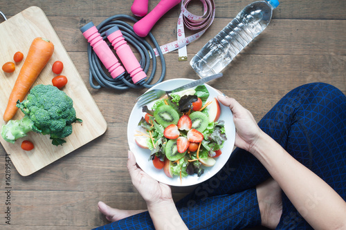 Woman in sportwear holding a dish of fresh salad with strawberries and kiwi, Healthy lifestyle