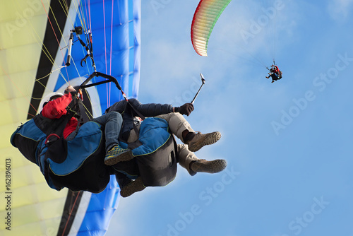 Dwie tandemowe paralotnie latają na tle błękitnego nieba, tandemowe paralotniarstwo prowadzone przez pilota