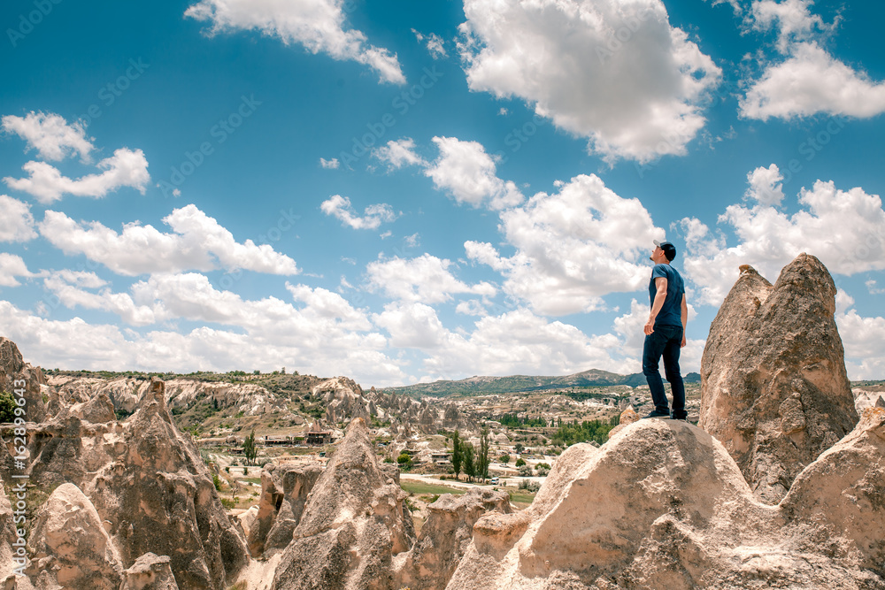 A man at the top of a hill in Cappadocia in Turkey looks up to the amazing clouds. Travel, success, freedom, achievement.