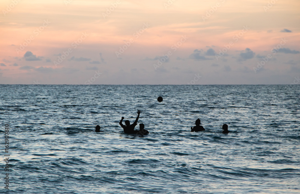 Teenagers Playing Ball in Ocean at Dusk
