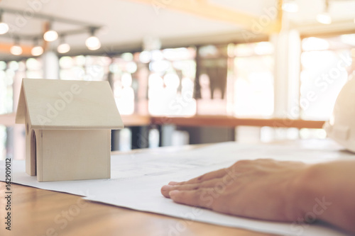 Image of engineer or architectural project, Close up of small house model and engineer's hand is laying on BluePrint with Engineering tools on workplace, Construction concept