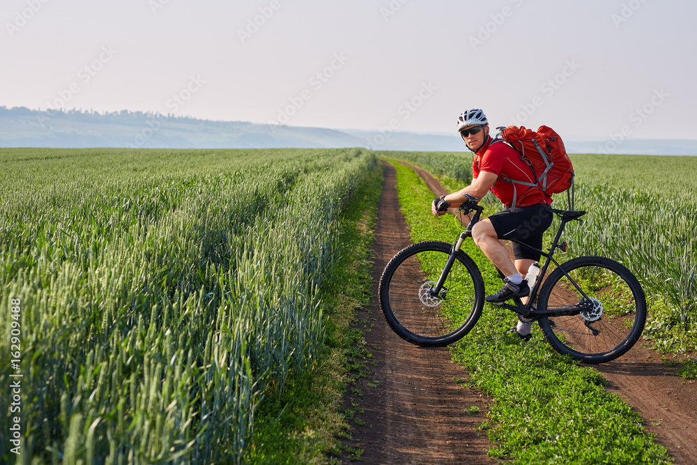 Fototapeta premium Young cyclist riding bicycle on the road on green field.