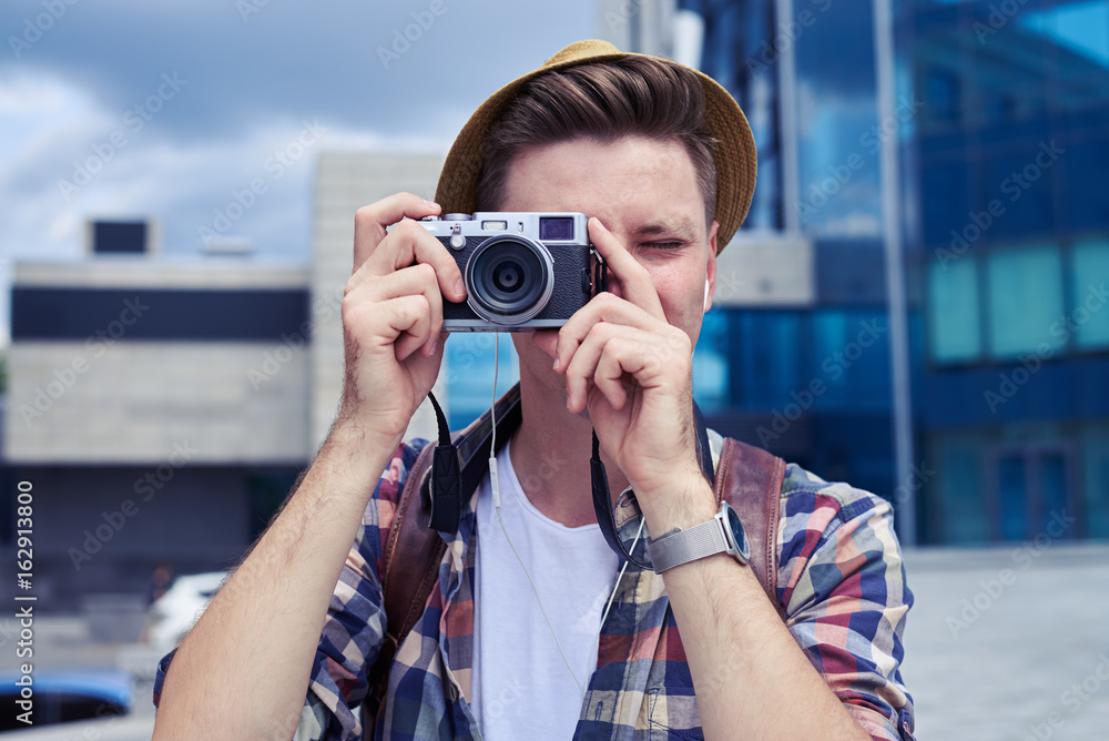 Cheerful young man in hat using old vintage photo camera
