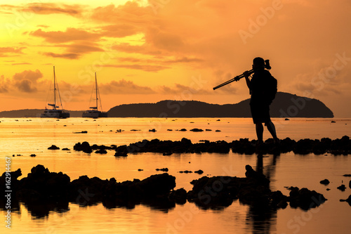 sillhoutte of photographer take tripod for shooting picture of boat in sea