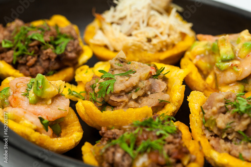 Plantain cups filled with different types of stuffing on black ceramic dish photo