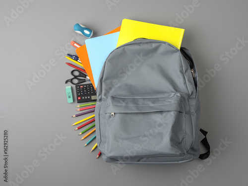 Top view of a backpack and school supplies on grey wooden table