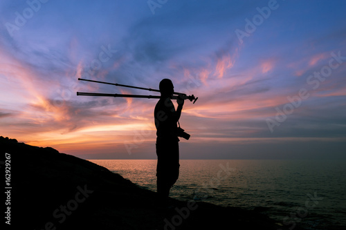 Silhouette of a photographer or traveler with tripod standing on stone ,sunset time.