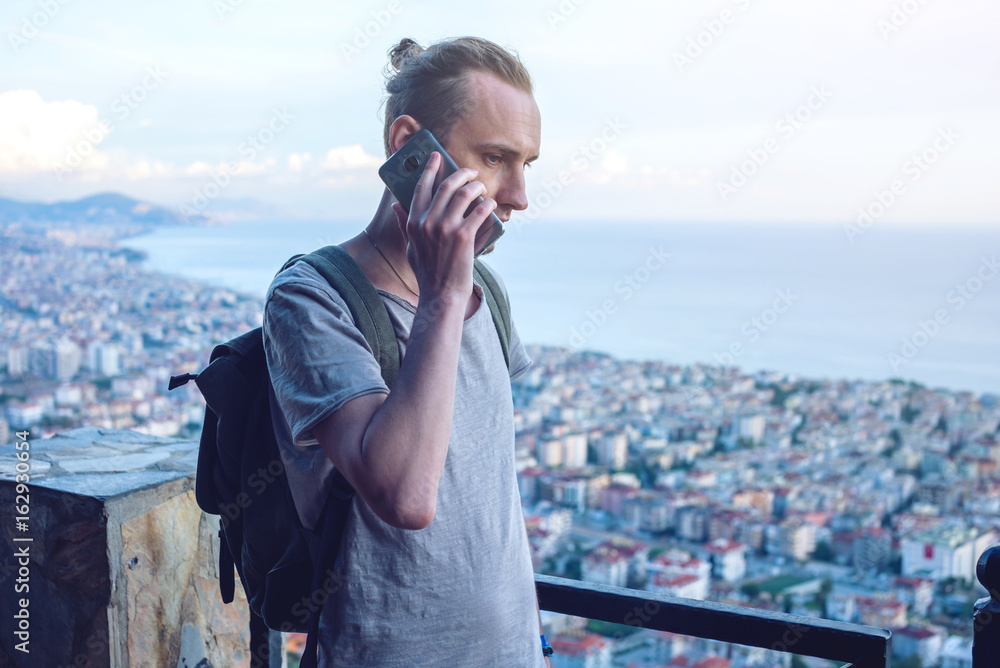 Man traveler with backpack talking on the phone on background of the city.
