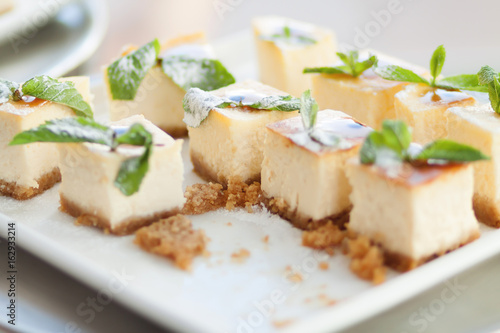 Appetizing cheesecake with mint leaves. Delicious sliced ​​dessert on white plate.