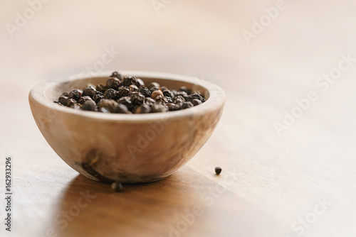 black dry pepper in wooden bowl on table