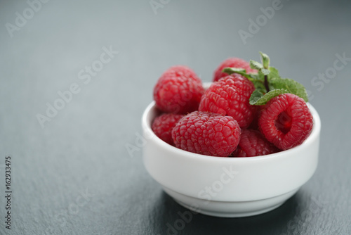 fresh raspberries with mint leaves in white bowl on slate board