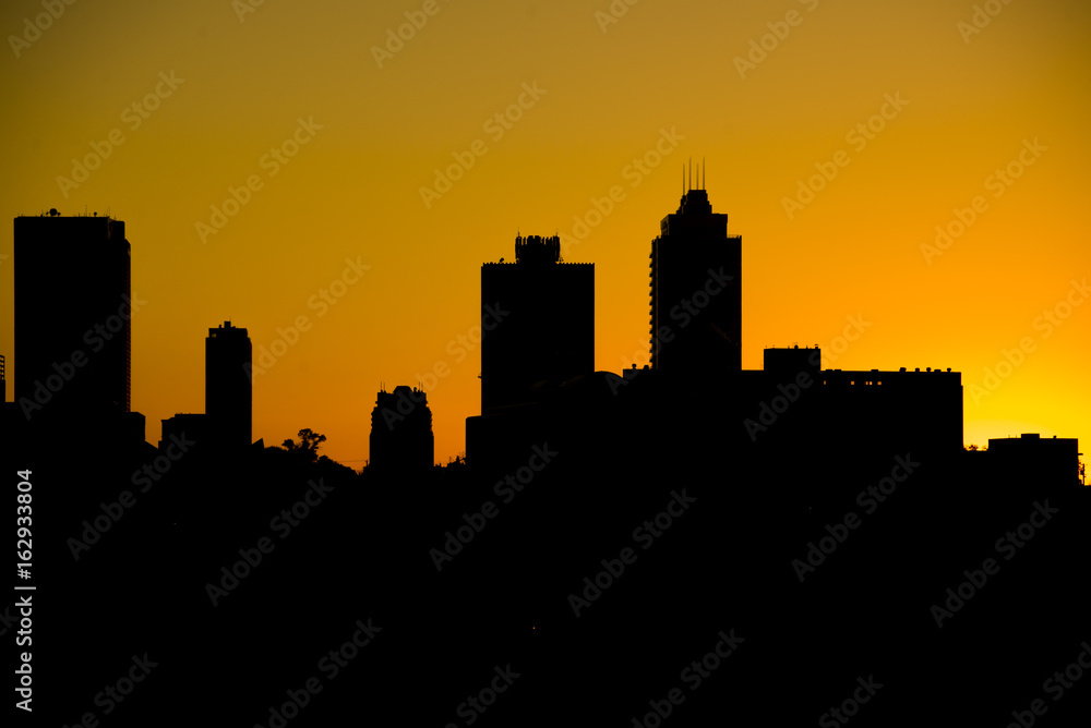 Silhouette of city skyline against orange setting sun