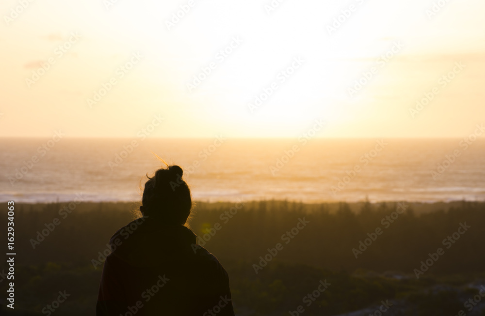 Silhouette of young woman looking out at sunset on pacific coast of Oregon Silhouette of young woman looking out at sunset on pacific coast of Oregon