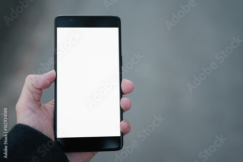 man hand holding smartphone with white screen outdoors with asphalt blurred background photo