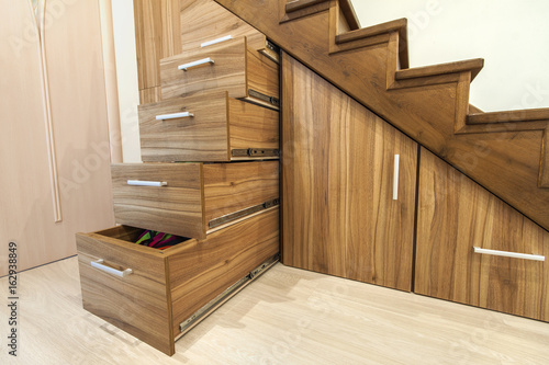 Modern architecture interior with luxury hallway with glossy wooden stairs in modern storey house. Custom built pullout cabinets on glides in slots under stairs