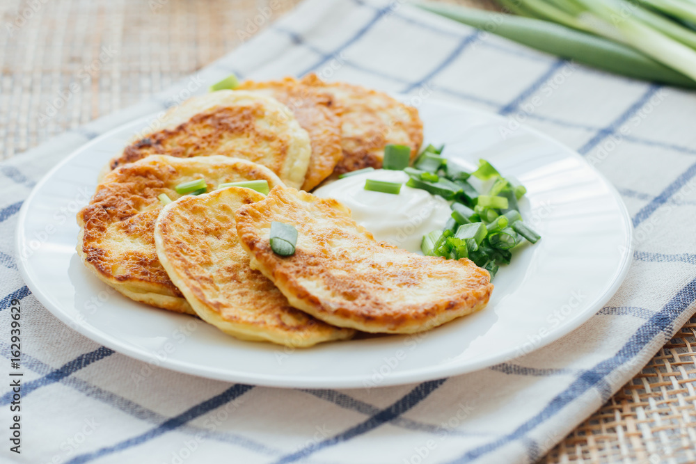 Vegetable fritters with sour cream and chopped leek on white plate 