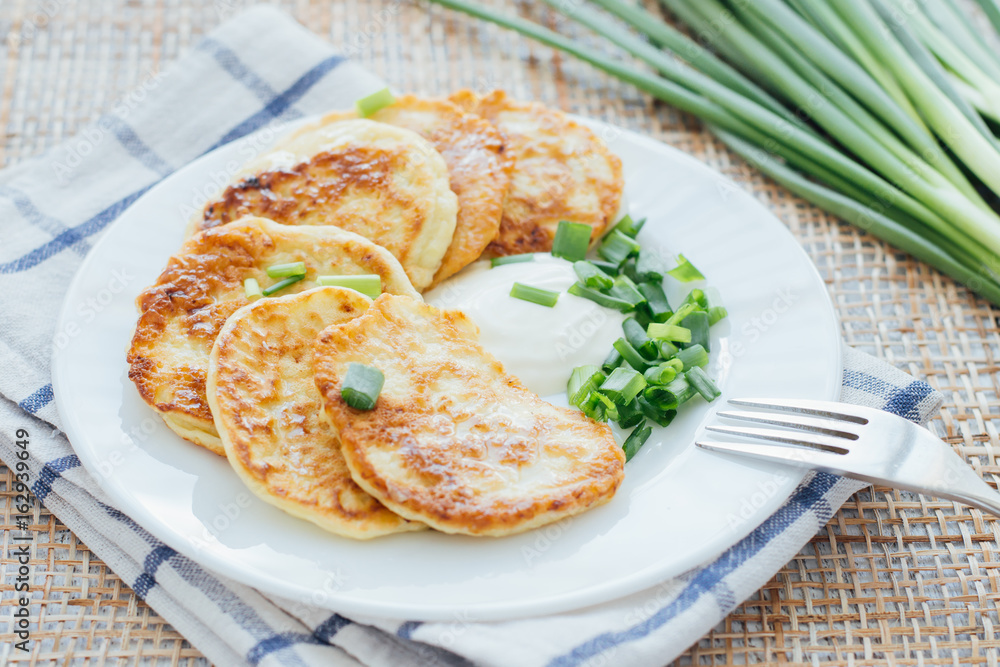 Vegetable fritters with sour cream and chopped leek on white plate Vegetable fritters with sour cream and chopped leek on white plate