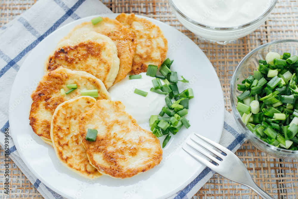 Vegetable fritters with sour cream and chopped leek on white plate 