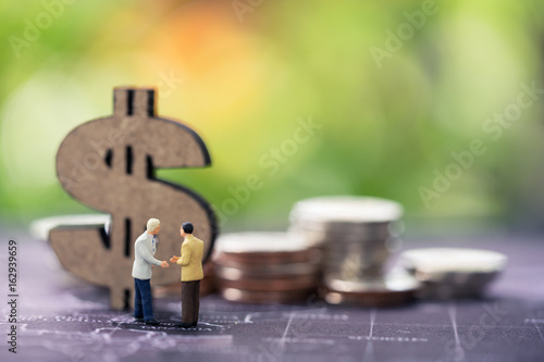 Miniature people: business man making decision on world map in front of wooden dollar sign and coins stacks, success, dealing, greeting and partner concept.