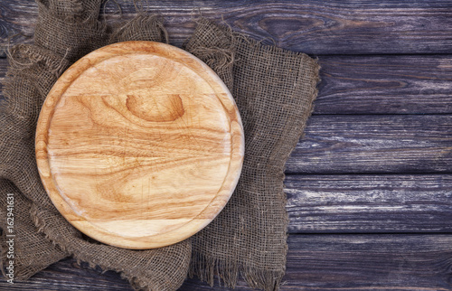 Round cutting board on old wooden texture background. Top view. Copy space.