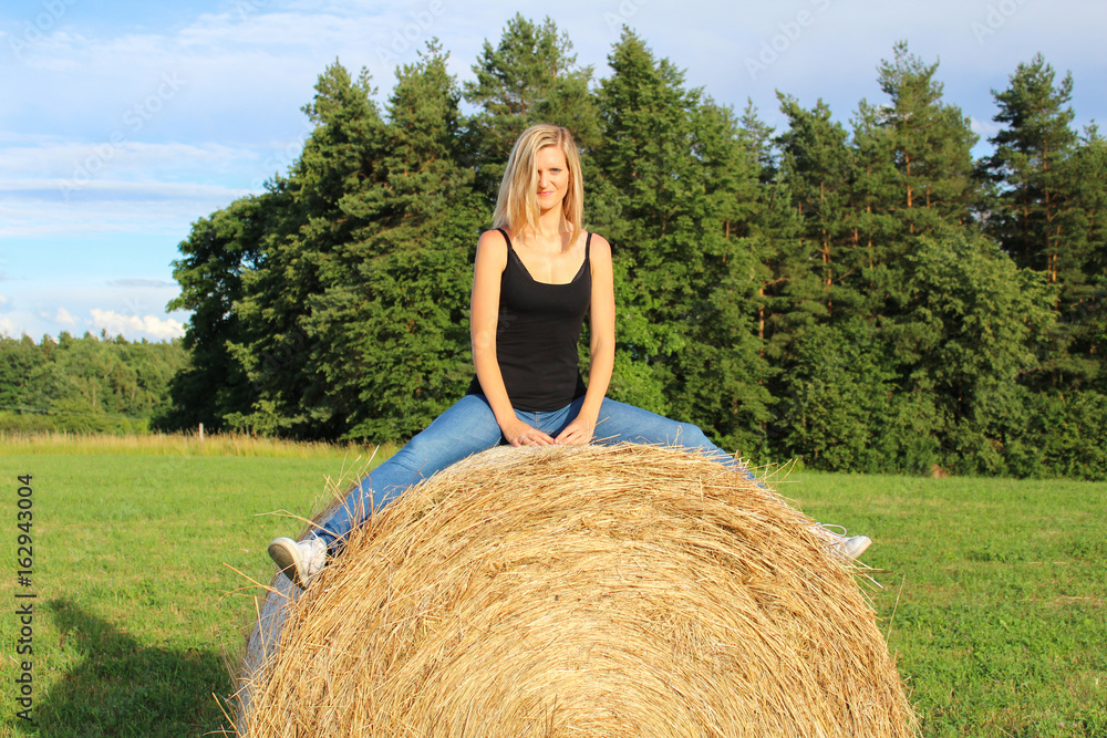 Young girl on straw bale and green meadow Young girl on straw bale and green meadow