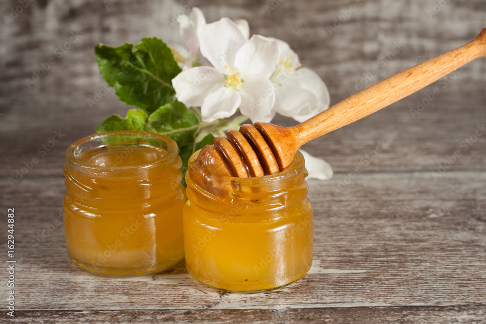 Honey dripping from a wooden honey dipper in a jar on wooden grey rustic background Honey dripping from a wooden honey dipper in a jar on wooden grey rustic background
