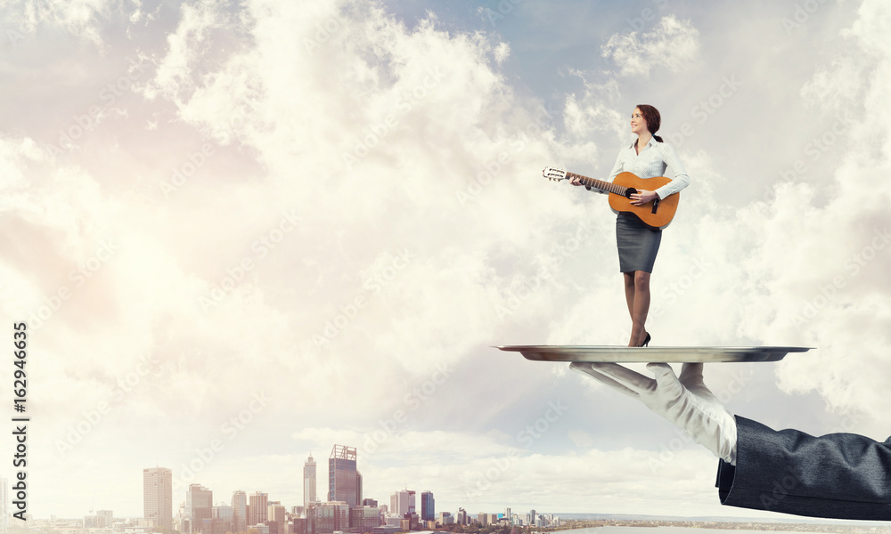 Attractive businesswoman on metal tray playing acoustic guitar against cityscape background Attractive businesswoman on metal tray playing acoustic guitar against cityscape background