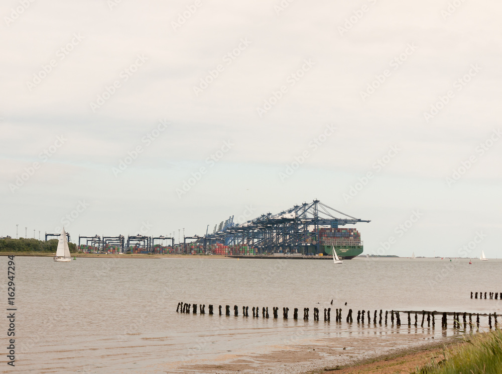 Fototapeta premium Stock Photo - blue sea structure cranes at cargo dock loading in distance felixstowe essex
