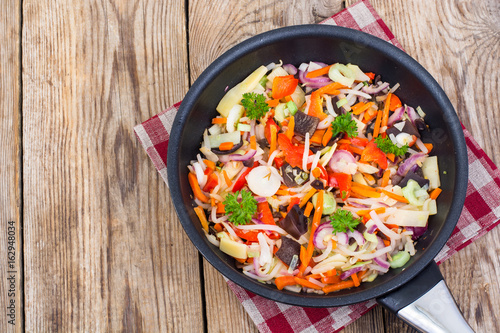 Frozen cooked vegetable mix in frying pan on wooden background, 