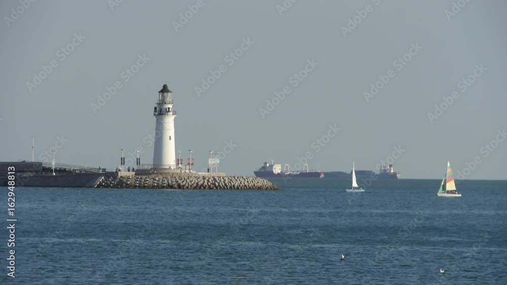 Sailboat sailing in sea,relying on lighthouse dam at dusk.water surface. Sailboat sailing in sea,relying on lighthouse dam at dusk.water surface.